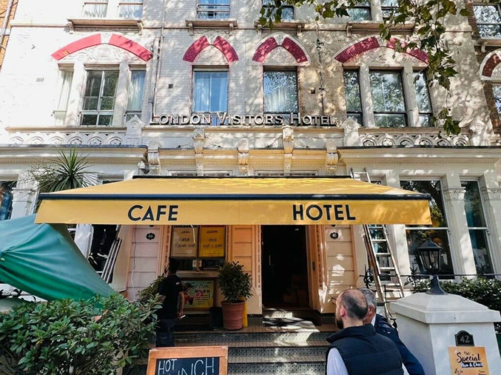 the entrance to london visitors hotel, above which is a yellow awning with the signs 'cafe' and 'hotel'
